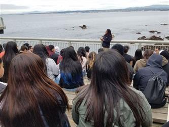 students sitting on benches looking out at bay with rocks and across to mountains